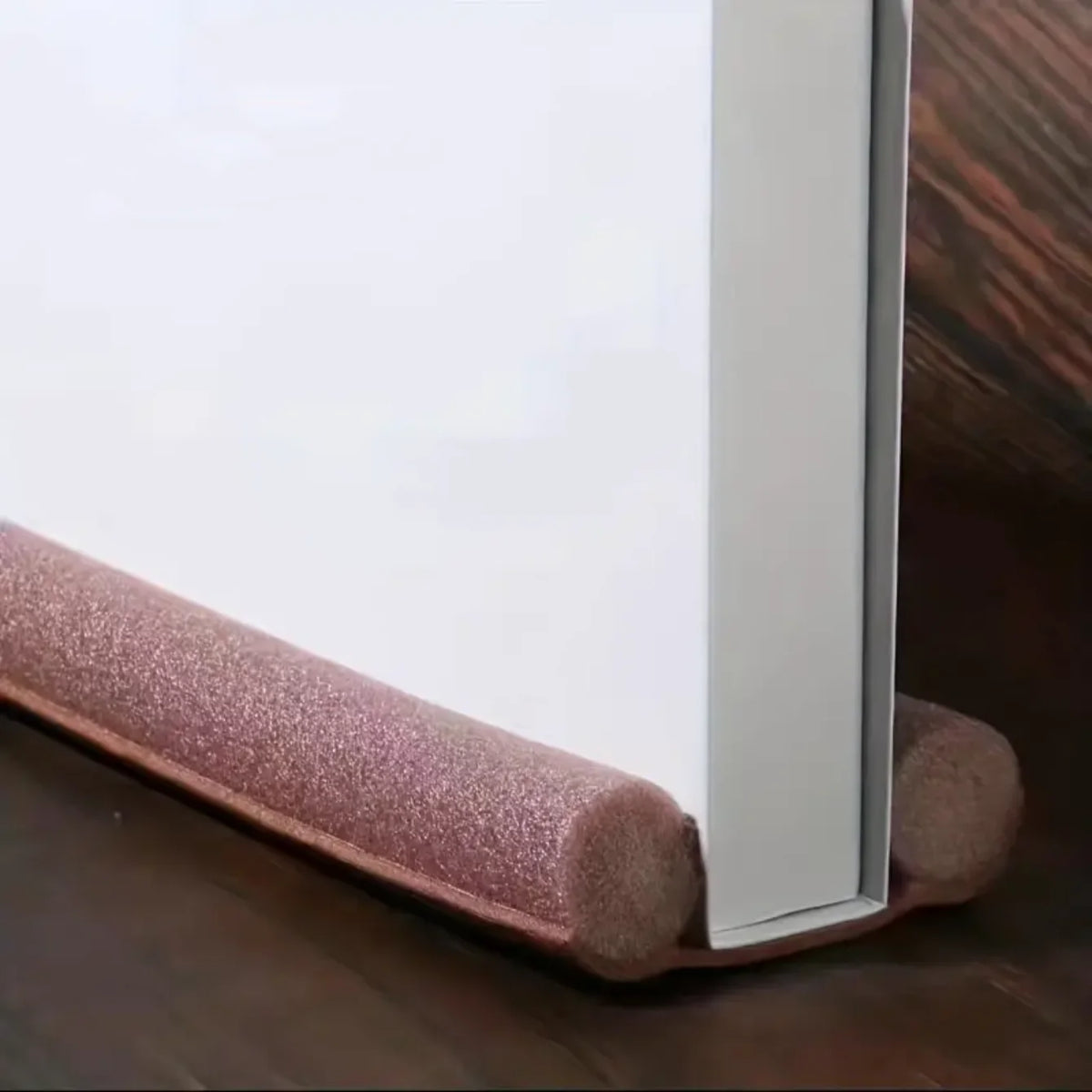 A white door and window sealing strip with a pink textured foam profile resting on a wooden surface.