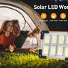 A portable solar LED work light is shown outdoors next to a tent, with two people in the background.