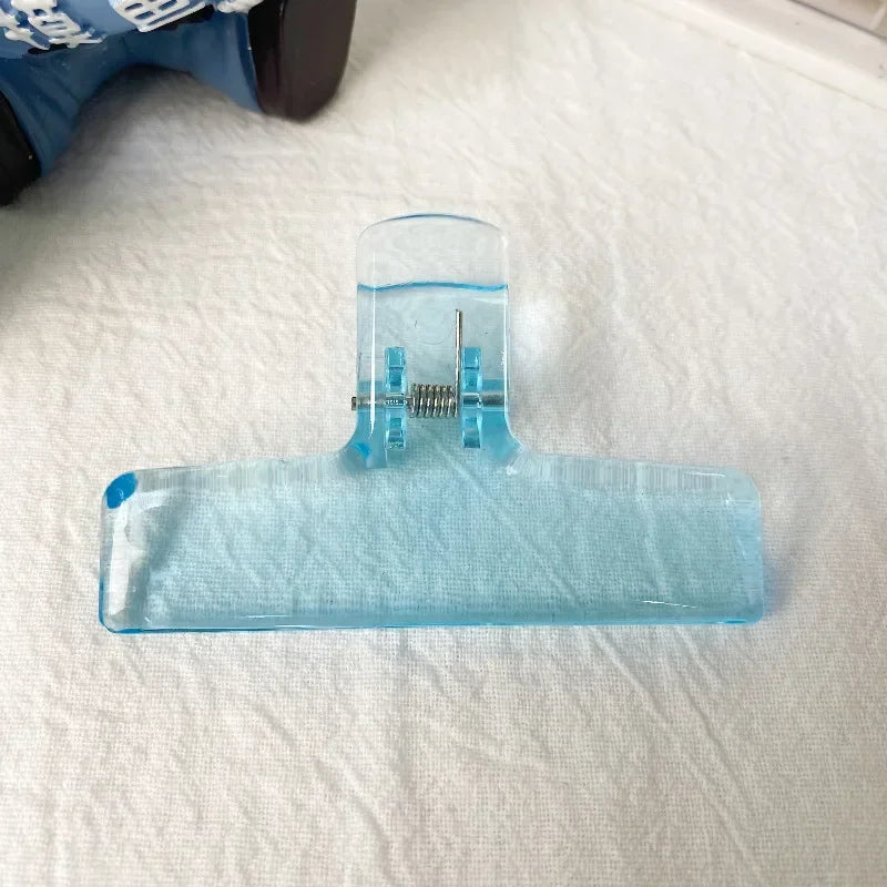 Klares Acryl-Federclipwerkzeug mit flacher Basis und vertikalem Halter auf weißem Tuch.