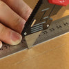 A hand is using a retractable utility knife to mark a line on brown paper, demonstrating the tool's blade and scale.