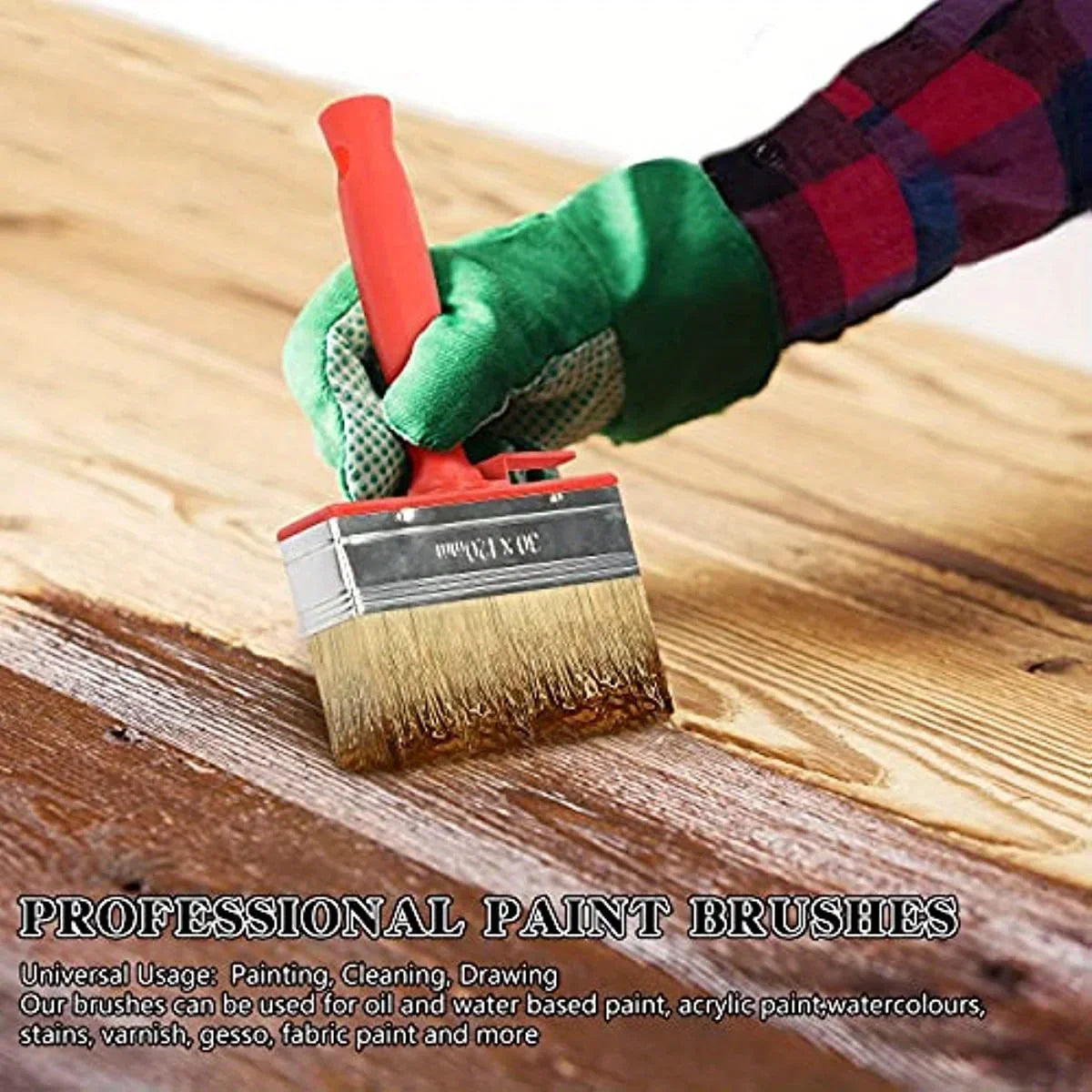 A hand holding a red handle and green brush applying paint on a wooden surface.