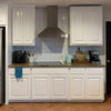 A kitchen cabinet and backsplash featuring white shaker cabinets and subway tiles with a gray hood above the countertop.