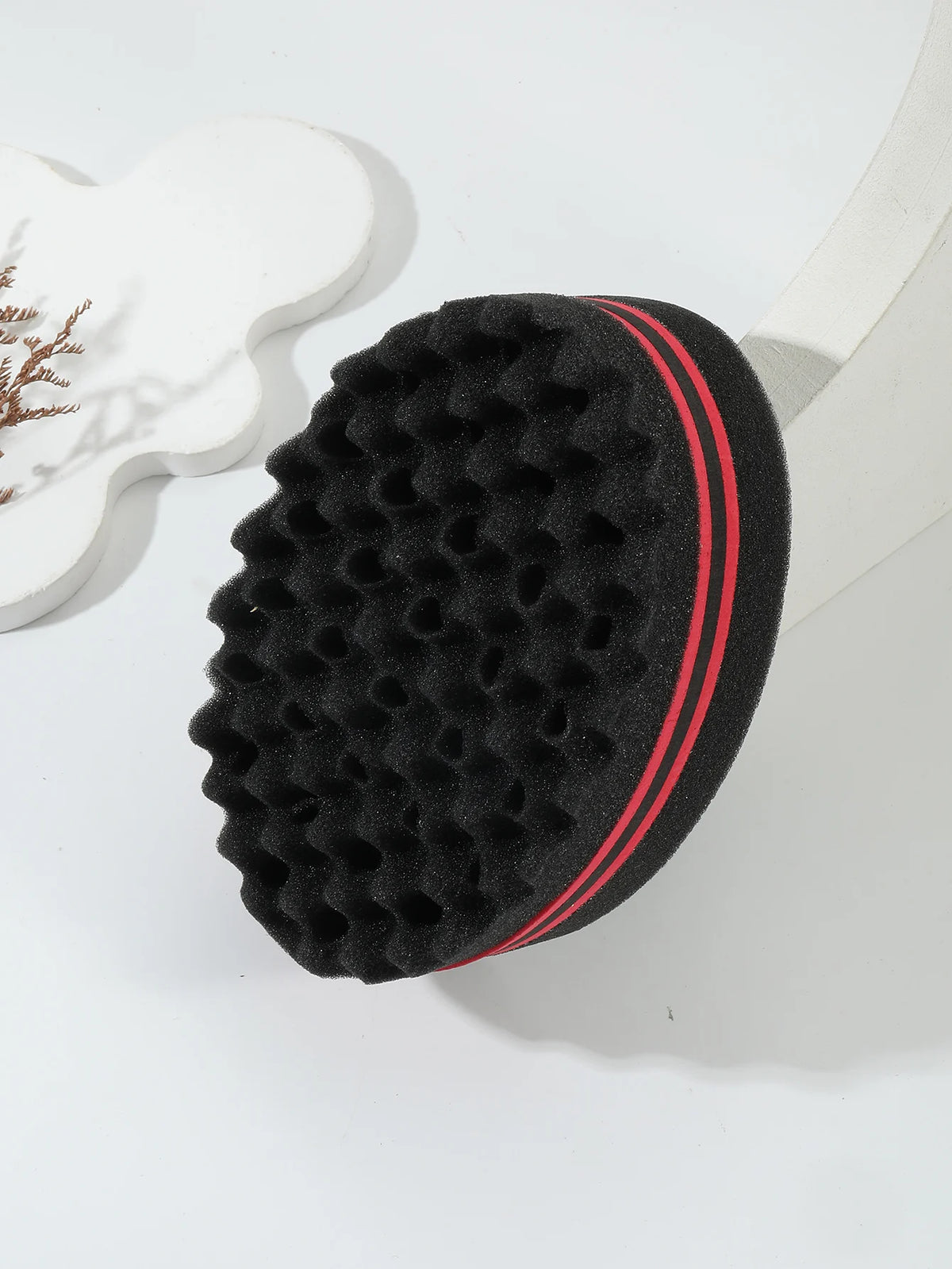 Un peigne de coiffure noir bouclé avec une bande rouge est montré à côté d'un objet en plastique blanc.