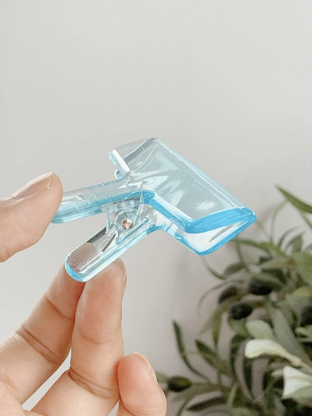 Eine Hand hält eine transparente Acryl-Federklammer vor einem hellen Hintergrund.