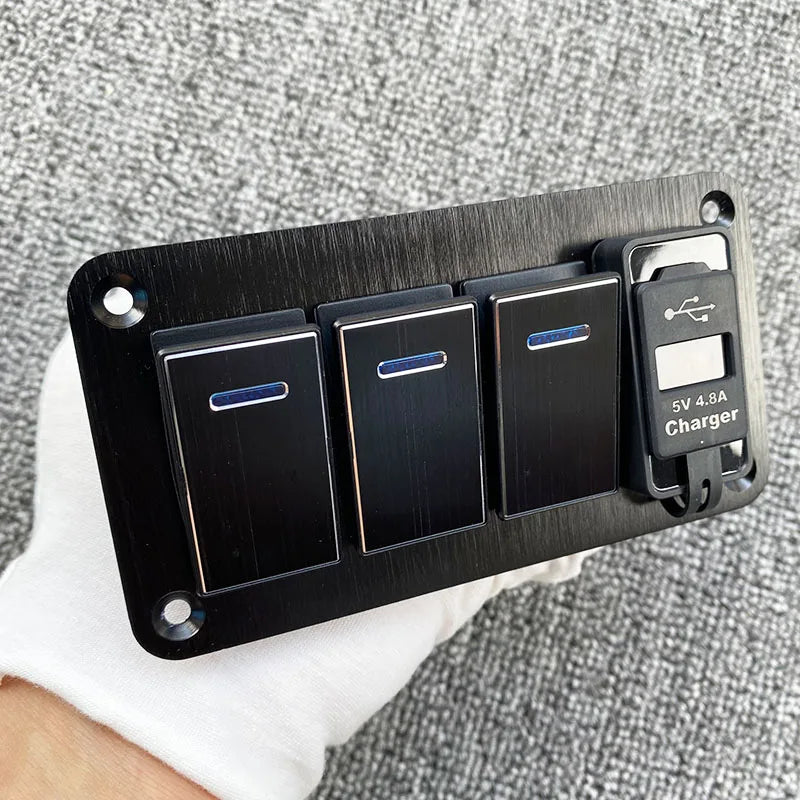 Un panneau noir avec trois cellules solaires et un chargeur 5V 4.8A est tenu dans une main sur un fond de tissu gris.