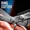 A hand holds a silver ring cutter tool, showing the blade and scale markings.