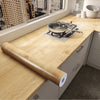 A roll of wood grain vinyl wall contact paper is placed on a light wood countertop next to a stovetop.