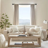 A living room scene featuring a light beige sofa, sheer curtains, and wooden furniture.
