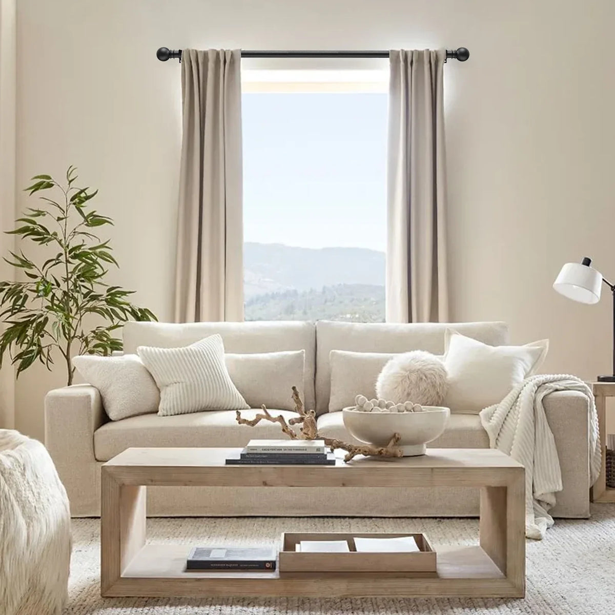 A living room scene featuring a light beige sofa, sheer curtains, and wooden furniture.