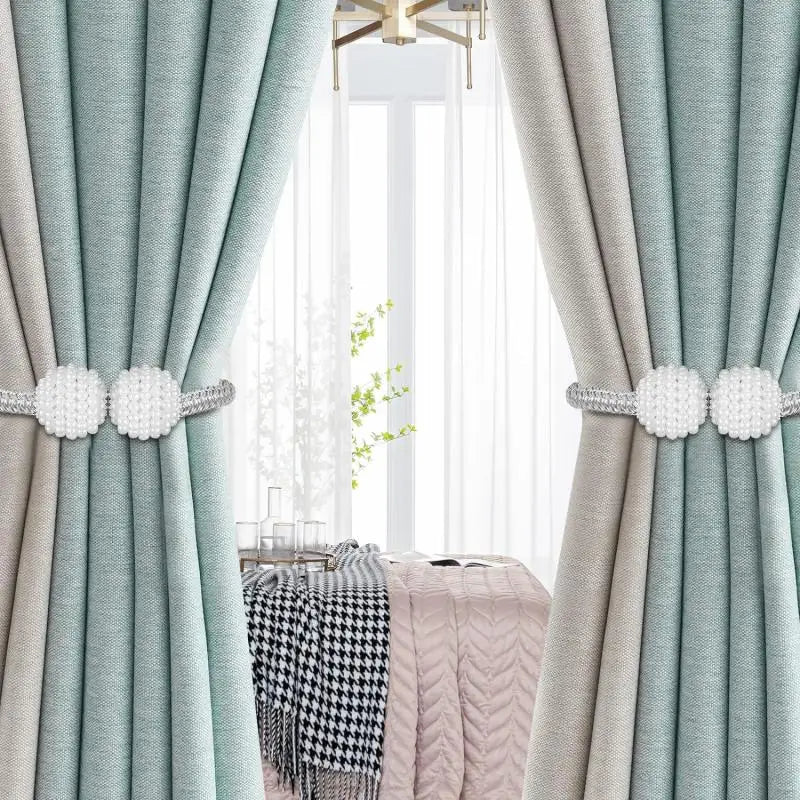 Hellblaue und beige Stoffvorhänge mit Perlmutt-Magnetklammern, die eine helle Fensteransicht einrahmen.