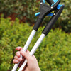 A hand is holding a blue and black foldable silicone garbage grabber tool against a blurred green outdoor background.