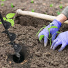 A hand wearing a purple glove is using a heavy-duty spiral garden auger to create a hole in dark soil for planting.