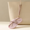 A light pink PU leather eyeglasses case with a gold chain strap is shown against a beige handbag.