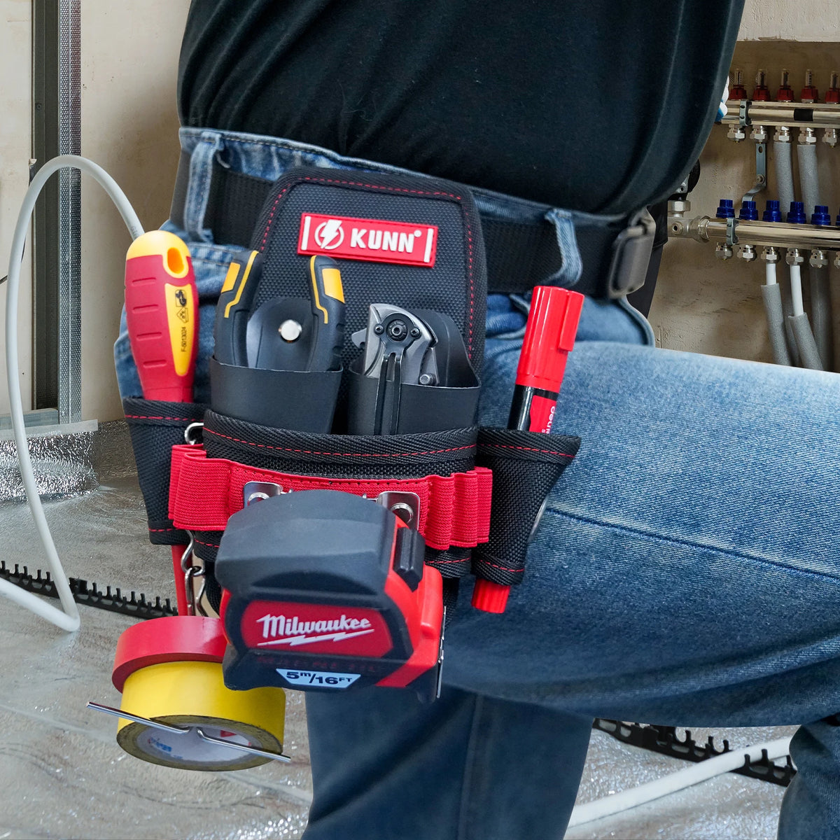 A red and black compact utility tool pouch with a belt clip is worn on a person's jeans.