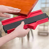 Hands are using a red plastic contour measuring ruler to measure or mark a surface.