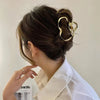 A woman is shown in profile with her hair styled in an elegant updo using gold S-shaped metal hair clips.