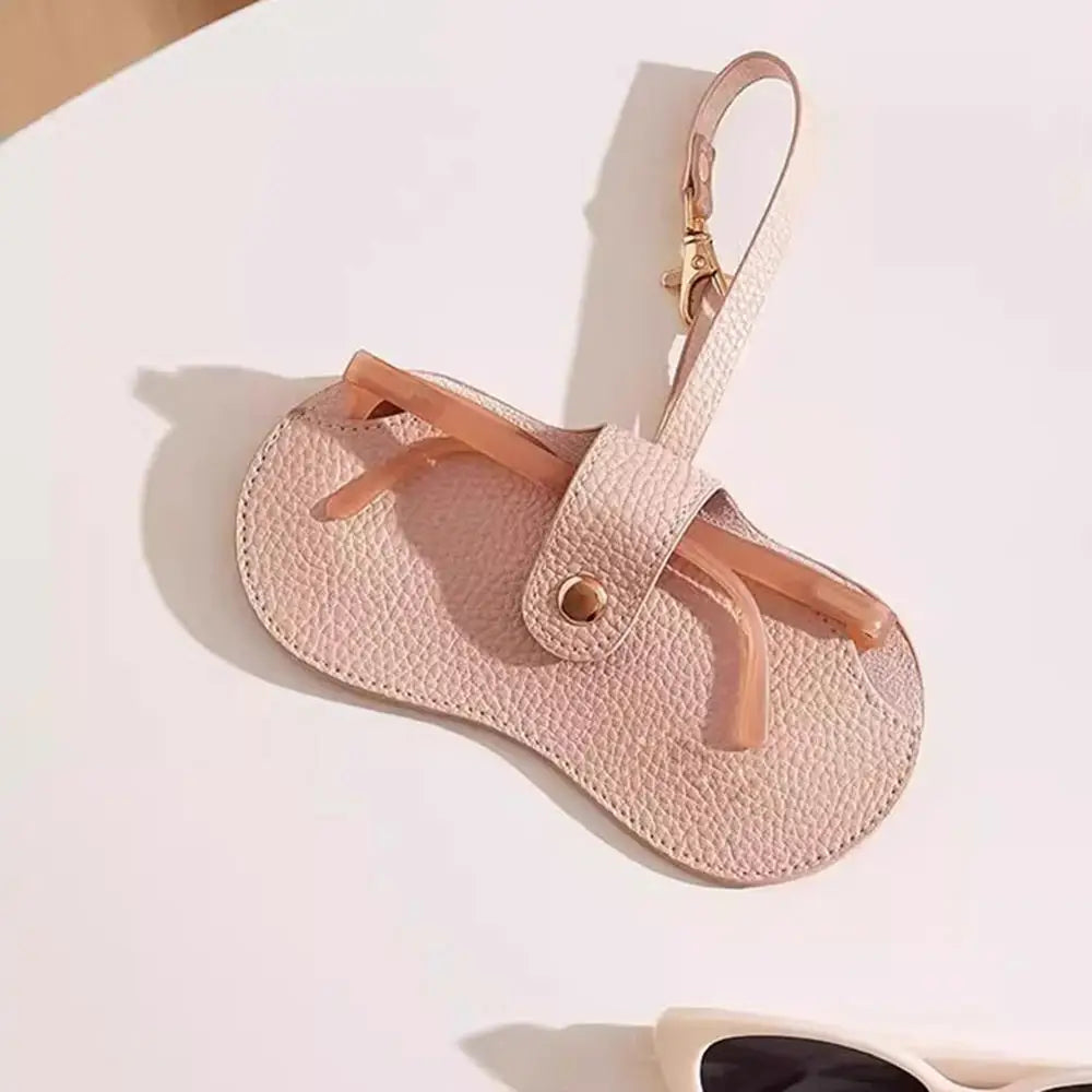 A light pink lychee pattern PU leather eyeglasses case with a tan strap and gold hardware.