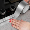 A hand is holding a roll of silver aluminum foil tape, demonstrating the product for pipe and leak sealing.