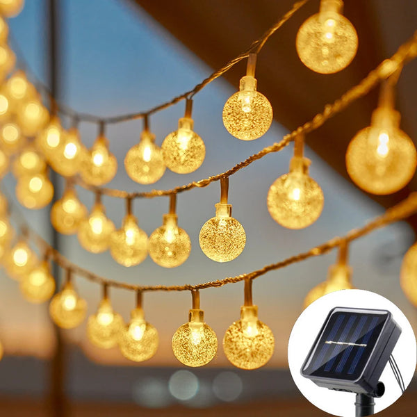 String lights with gold-colored fairy lights hanging outdoors, next to a solar panel.