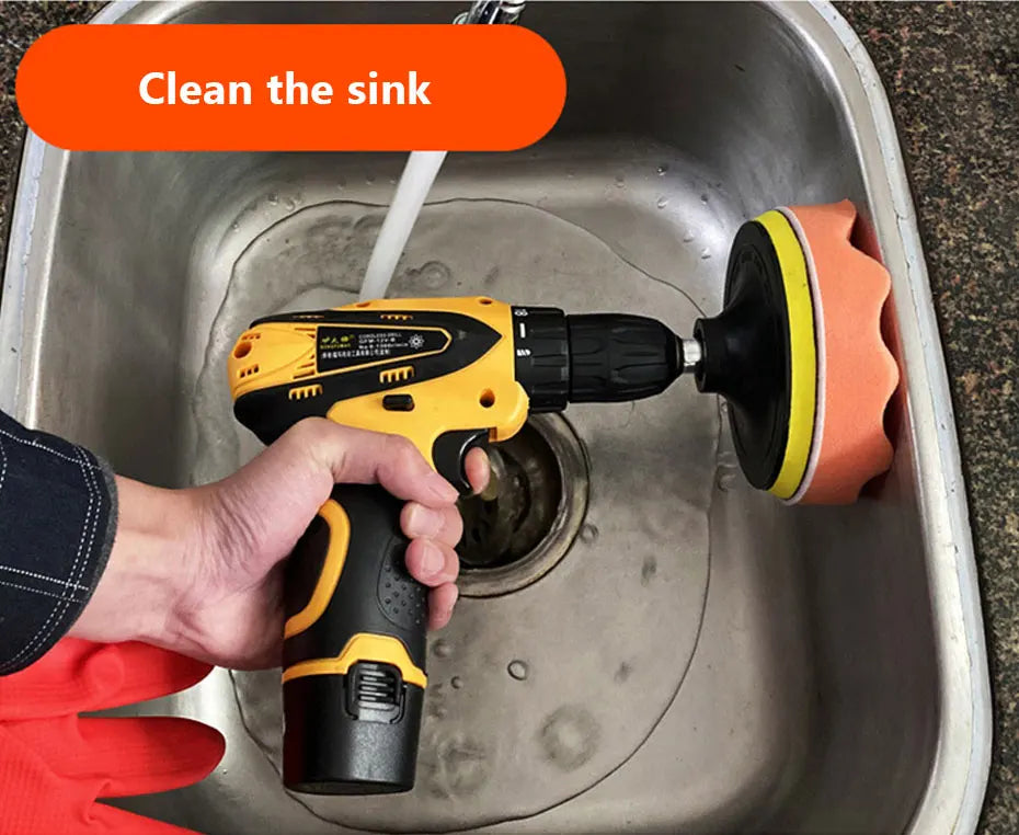A hand uses a yellow electric tool to clean a kitchen sink, with an orange cleaning pad attached.