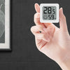 Una mano sostiene un termómetro digital blanco que muestra 28.5 grados Celsius y 59% de humedad.