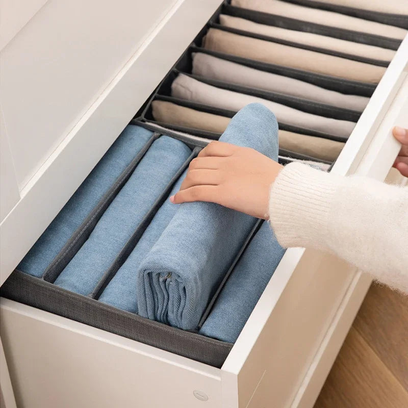 A hand is placing folded blue fabric storage towels into a white organizer box with multiple compartments.