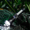 A black tactical LED flashlight is shown illuminating a wet, dark rock surface amidst falling rain.