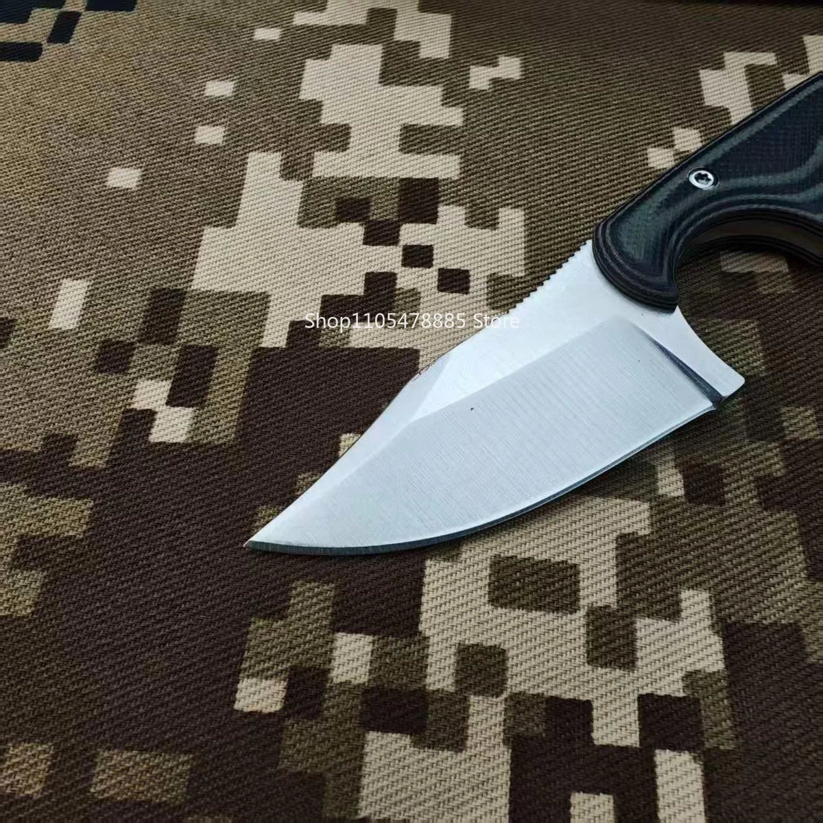 A silver utility knife with a black handle rests on a brown camouflage fabric.