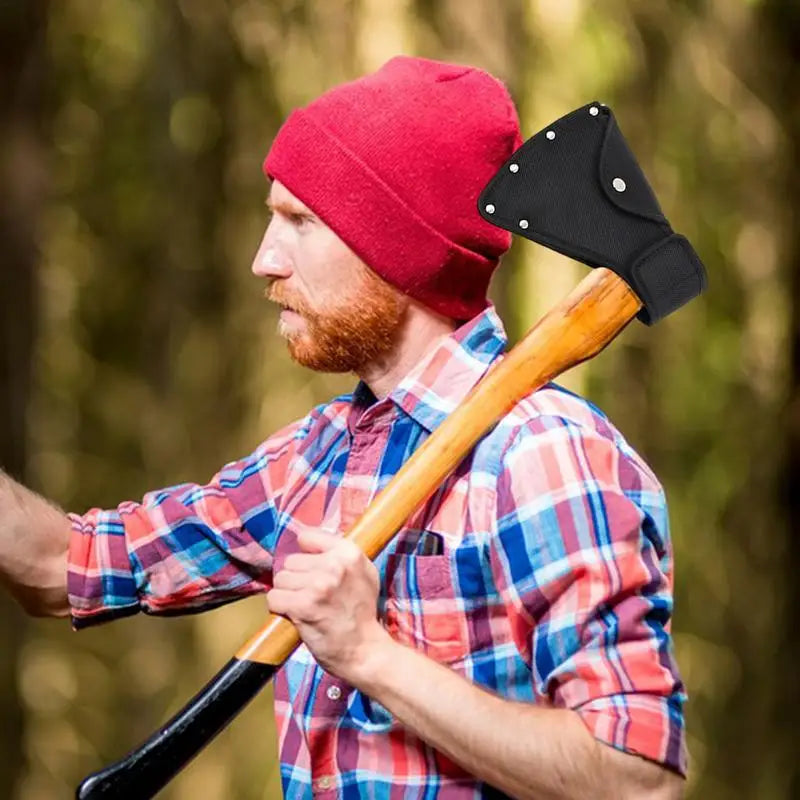 A bearded man wearing a red beanie holds a wooden axe with a black nylon blade cover in an outdoor setting.