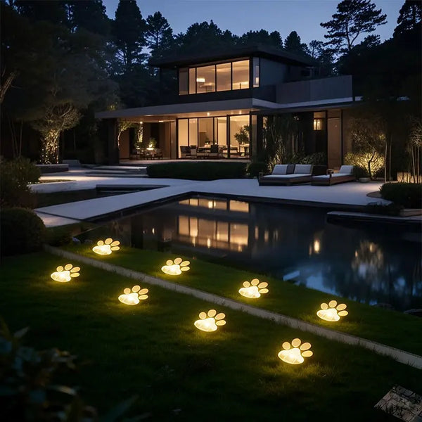 Outdoor pathway lights shaped like paw prints illuminating a lawn and reflecting in a water feature at dusk