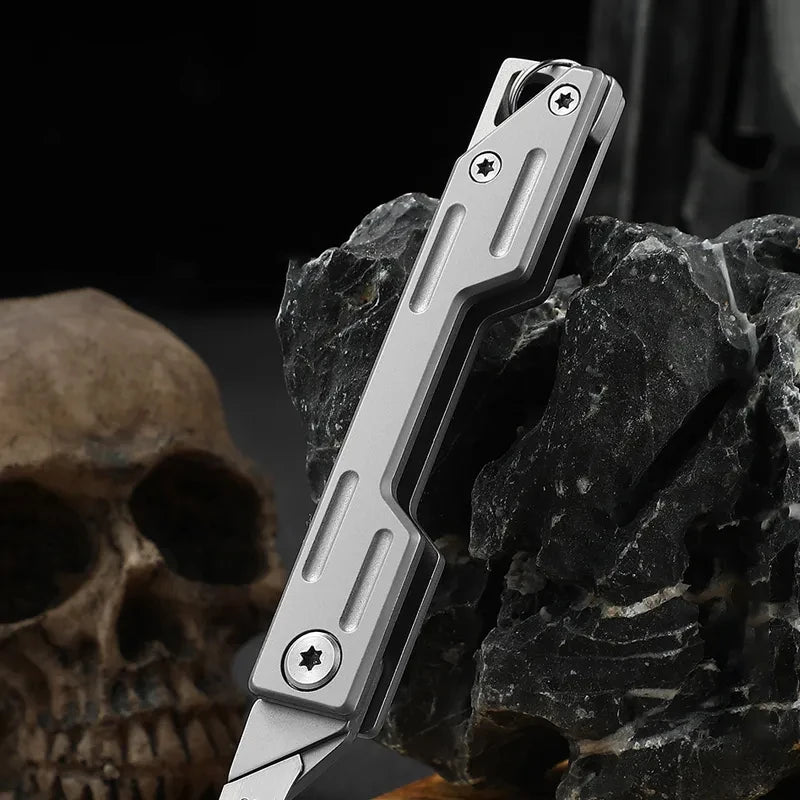 A silver multi-blade folding pocket knife kit is shown resting on a dark rock next to a human skull.