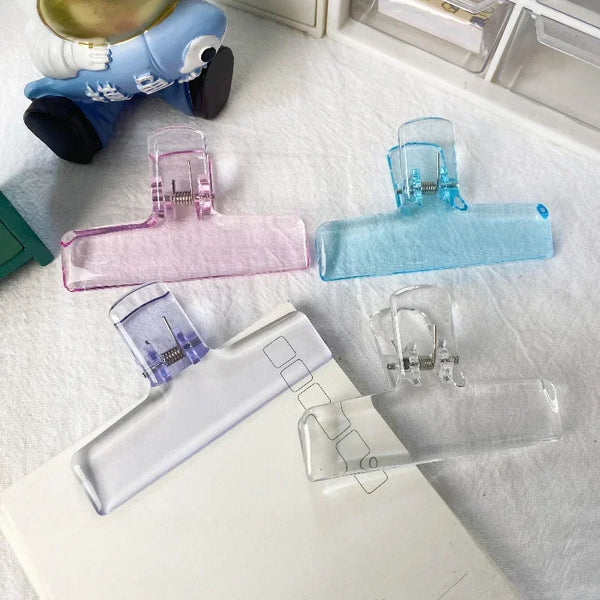 A collection of transparent acrylic spring paper clips in various colors, including pink, blue, and clear.