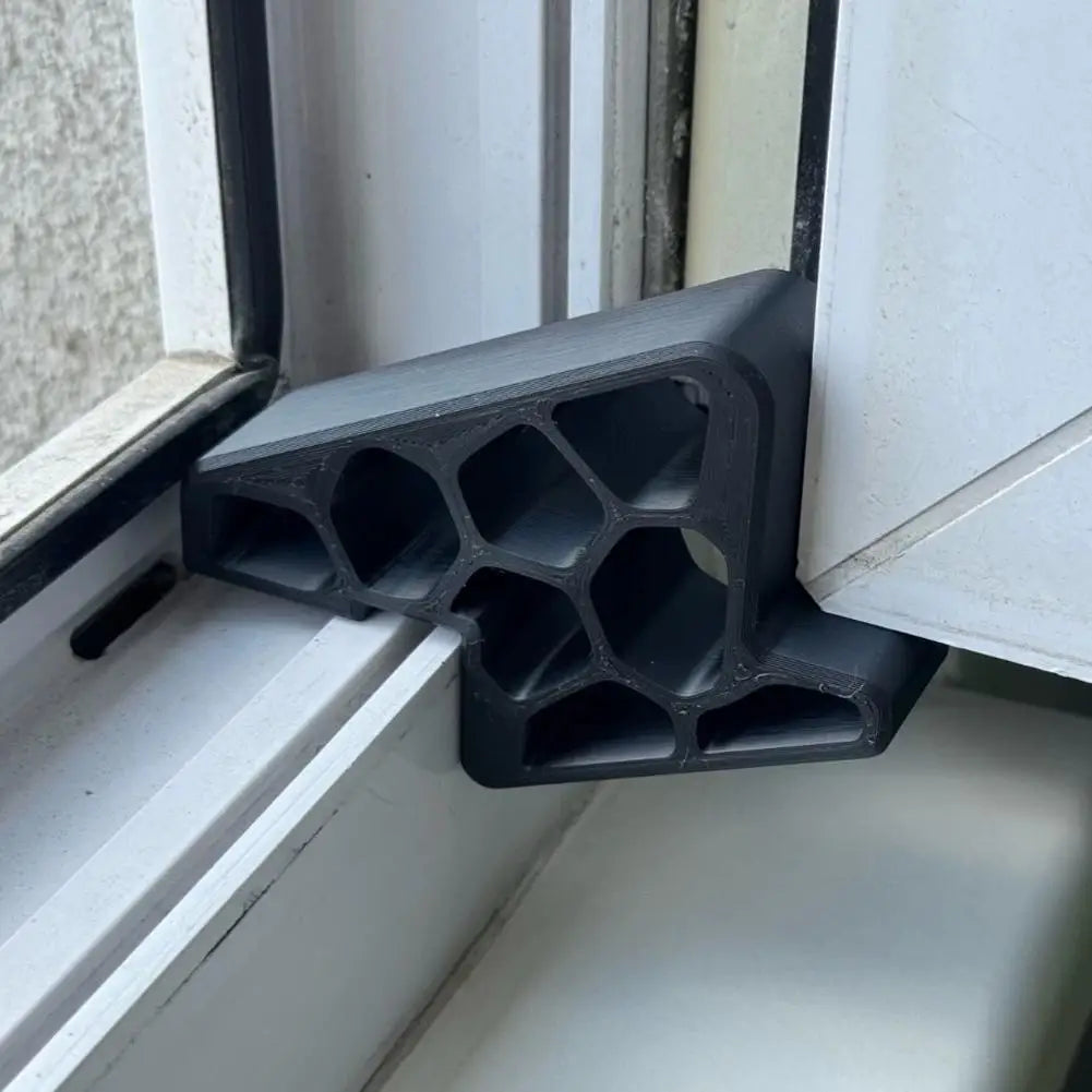 Stopper de puerta y ventana negro resistente al deslizamiento con estructura de panal, instalado en un marco blanco.