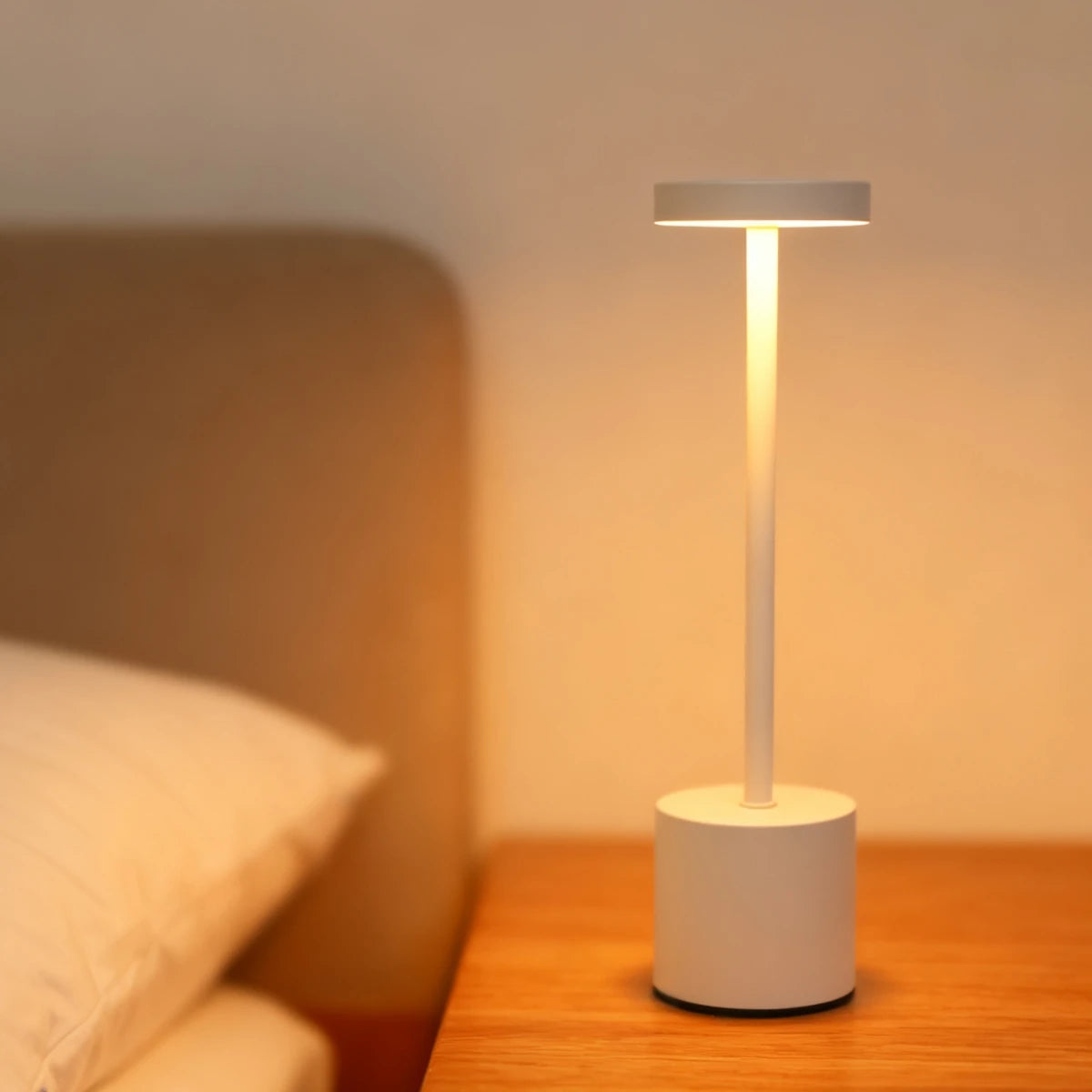 A modern white desk lamp with a cylindrical light and a square shade sits on a wooden surface.