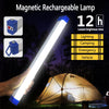 A hand holds a bright white magnetic rechargeable lamp illuminating a dark outdoor scene near a tent.