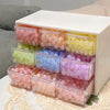 A white drawer organizer with four clear compartments filled with colorful round beads.