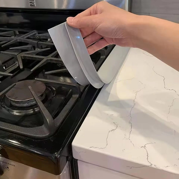 A hand is holding a silicone gas stove sealing strip over a black stovetop.