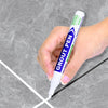 Une main tient un stylo réparateur de joint vert pour marquer les joints de carreaux sur une surface grise.
