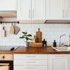 A kitchen countertop with wooden cutting boards, a sink, and white cabinets featuring brushed nickel and gold cabinet handles