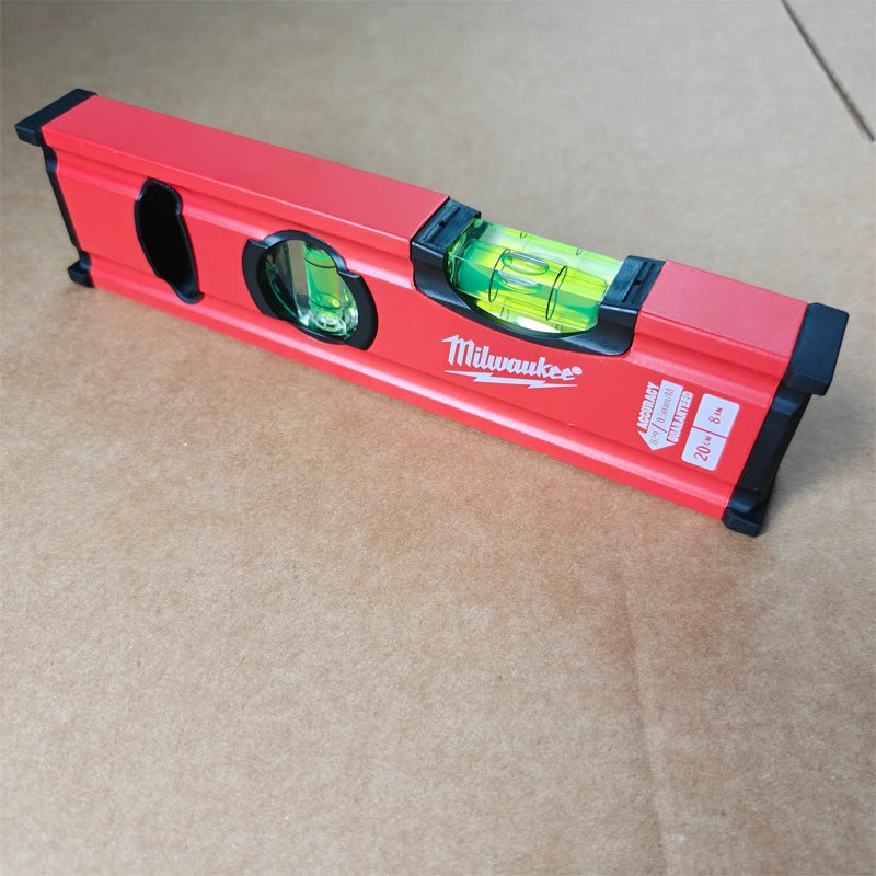 A red precision aluminum torpedo level set with a green liquid inside, resting on brown paper.