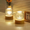 A glowing crystal ball night light with a deer silhouette decoration on a wooden base.