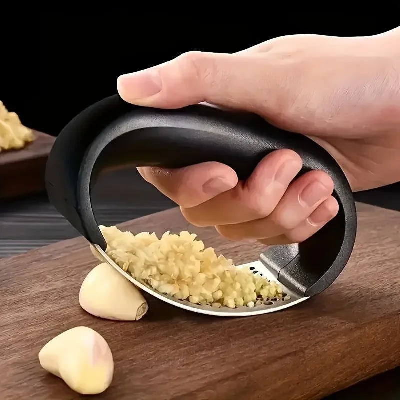 A hand is pressing garlic and ginger through a manual stainless steel press onto a wooden surface.