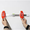 Hands hold an orange picture hanging level and angle measuring tool against a white surface with a ruler.