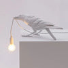 Weiße Harf-Vogelskulptur, beleuchtet durch eine flexible Leuchte, auf weißer Oberfläche.