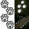 Four solar paw print pathway lights illuminating a stone walkway in a garden setting.