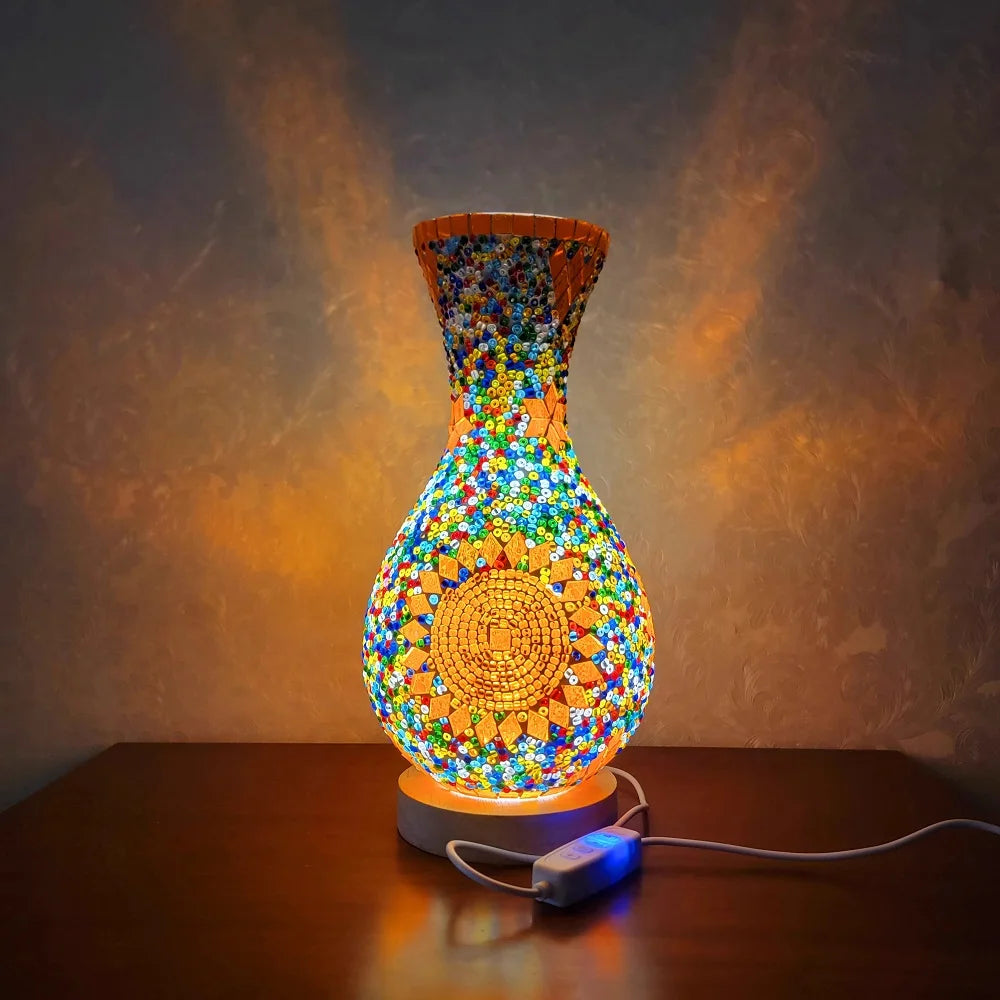 Una lámpara de mesa de vidrio vibrante con diseño texturizado y colorido, insertado a mano, ilumina una superficie de madera 