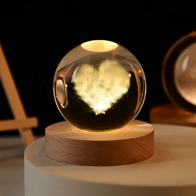 A glass crystal ball night light with a glowing heart shape inside, resting on a wooden base.