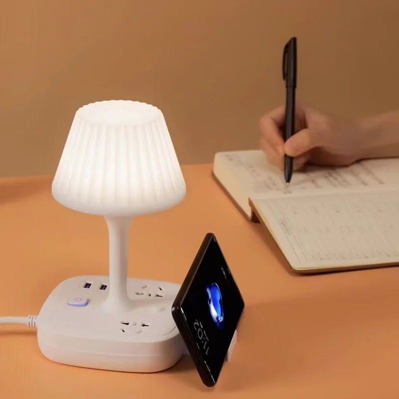 A white multi-functional conversion desk lamp with USB and AC outlets is shown next to a notebook and a pen.