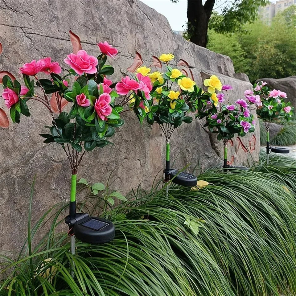 Solar LED azalea flowers in pink and yellow bloom on a green garden bed.