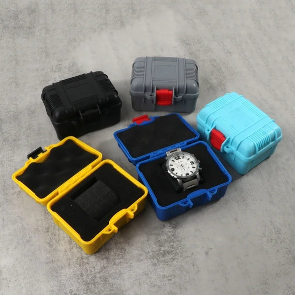 A collection of impact-resistant watch storage cases in black, gray, and blue, with one open case displaying a silver wristwa